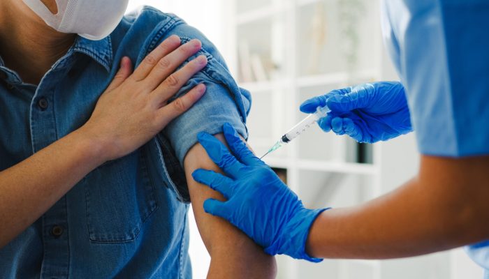 Young Asia lady nurse giving Covid-19 or flu antivirus vaccine shot to senior male patient wear face mask protection from virus disease at health clinic or hospital office. Vaccination concept.